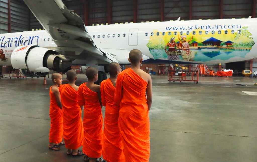 Young Buddhist monks viewing SriLankan Airlines aircraft with Navam Perahera cultural livery in Sri Lanka